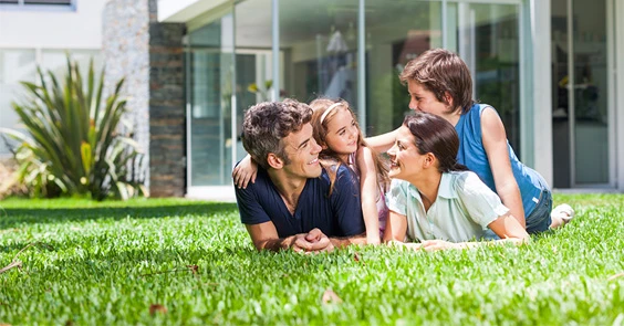 Family lying together on grass in front of a home
